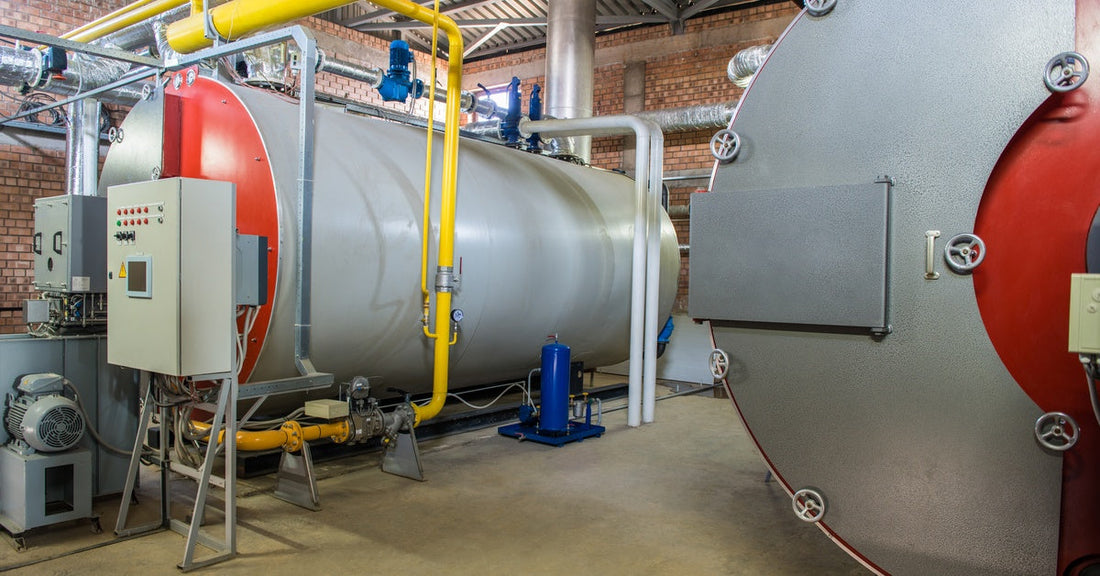 An industrial steam boiler room with two large stainless steel tanks connected through a network of pipes.