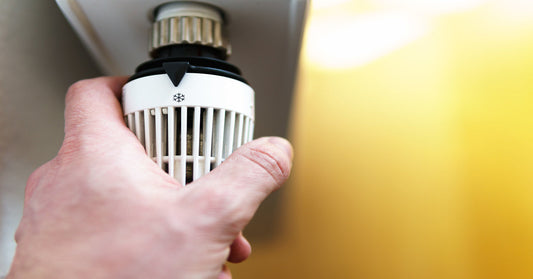 A close-up of a hand turning the radiator valve. The valve is white with a snowflake indicator setting on the base.