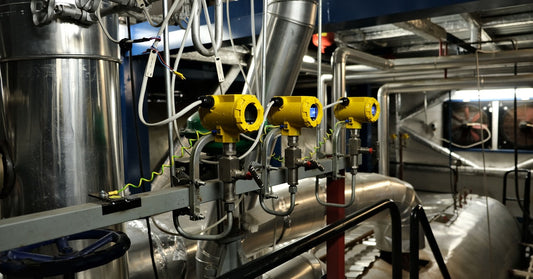 A dark boiler room with a stainless steel steam system that contains yellow valves and gauges. The gauge system is electric.