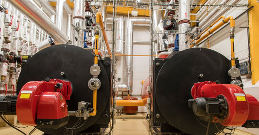 An industrial steam boiler room with two large black boiler tanks with red steam engines. There are yellow pipes around.