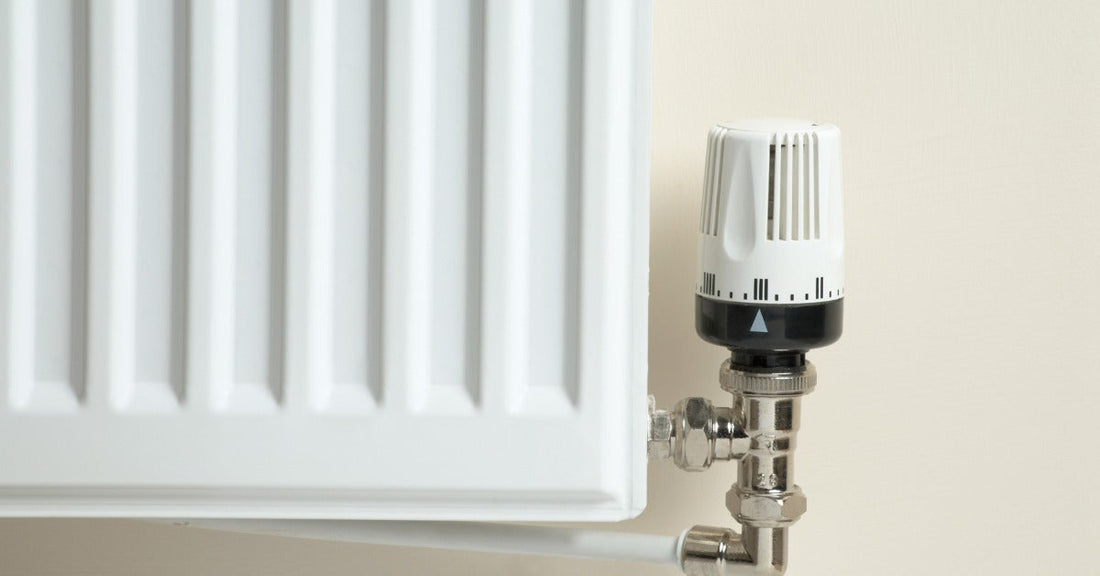 A close-up of a thermostatic radiator valve on a wall-mount radiator system. The valve is white with a dial.