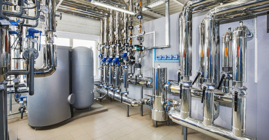 A commercial steam boiler room with new stainless steel pipework and boilers. There are blue gauges on the pipes.