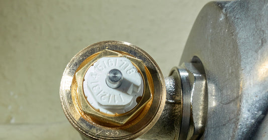 A close-up of a newly installed radiator valve on the end of a stainless steel pipe system. The cap is white.